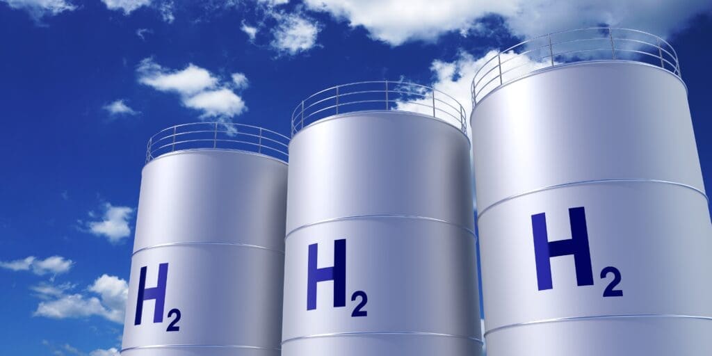 Three hydrogen storage tanks against a blue sky with clouds. Blue text reads H2 on each tank